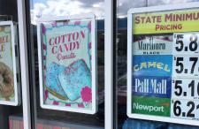 Sign on Gas Station with State Minimum Cigarette Pricing, next to flavored doughnut advertisements