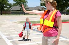 A crossing guard stopping traffic for a child to cross the street.